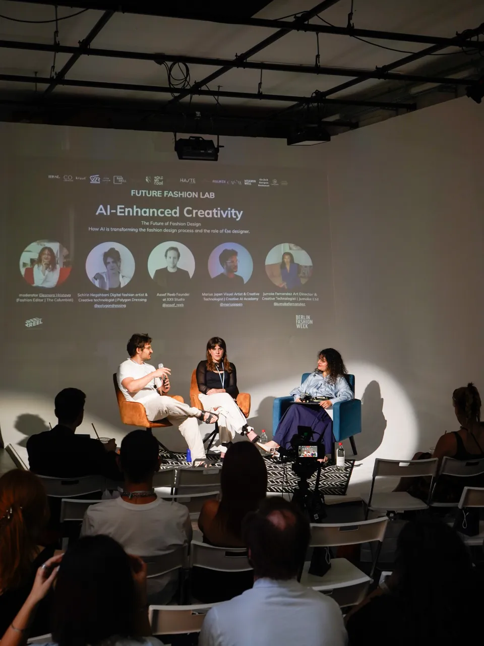 Panel discussion at Reel2Reel Studio during Future Fashion Lab — speakers on stage with exposed ceiling rig and white cyclorama, audience in the foreground